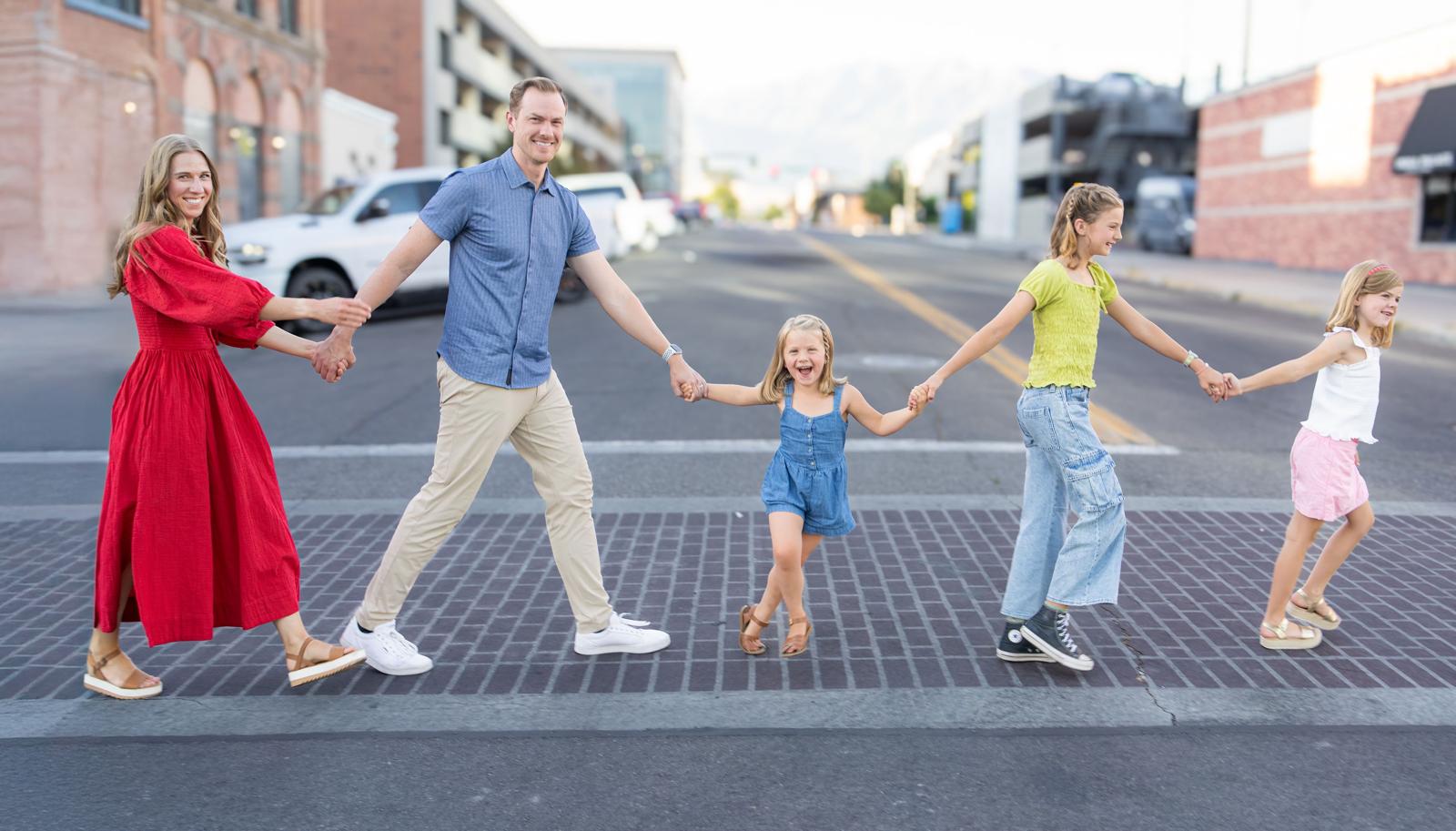 Family of five holding hands and walking across a city street