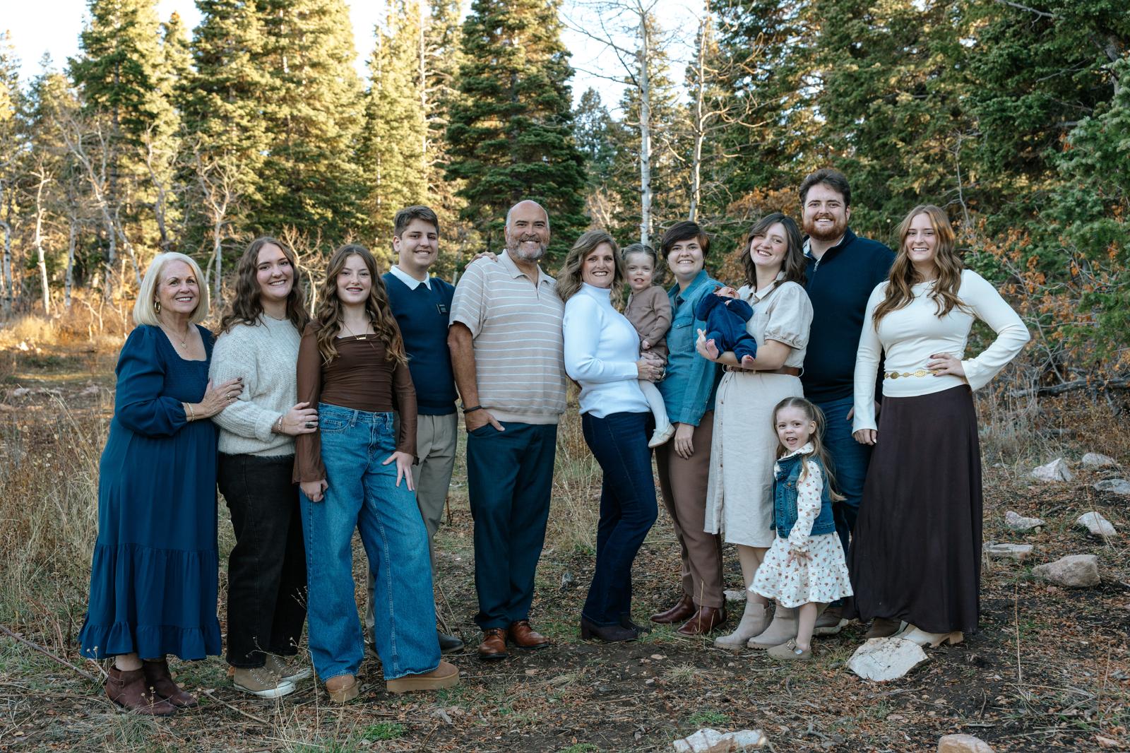Large family group posing together outdoors among pine trees in autumn