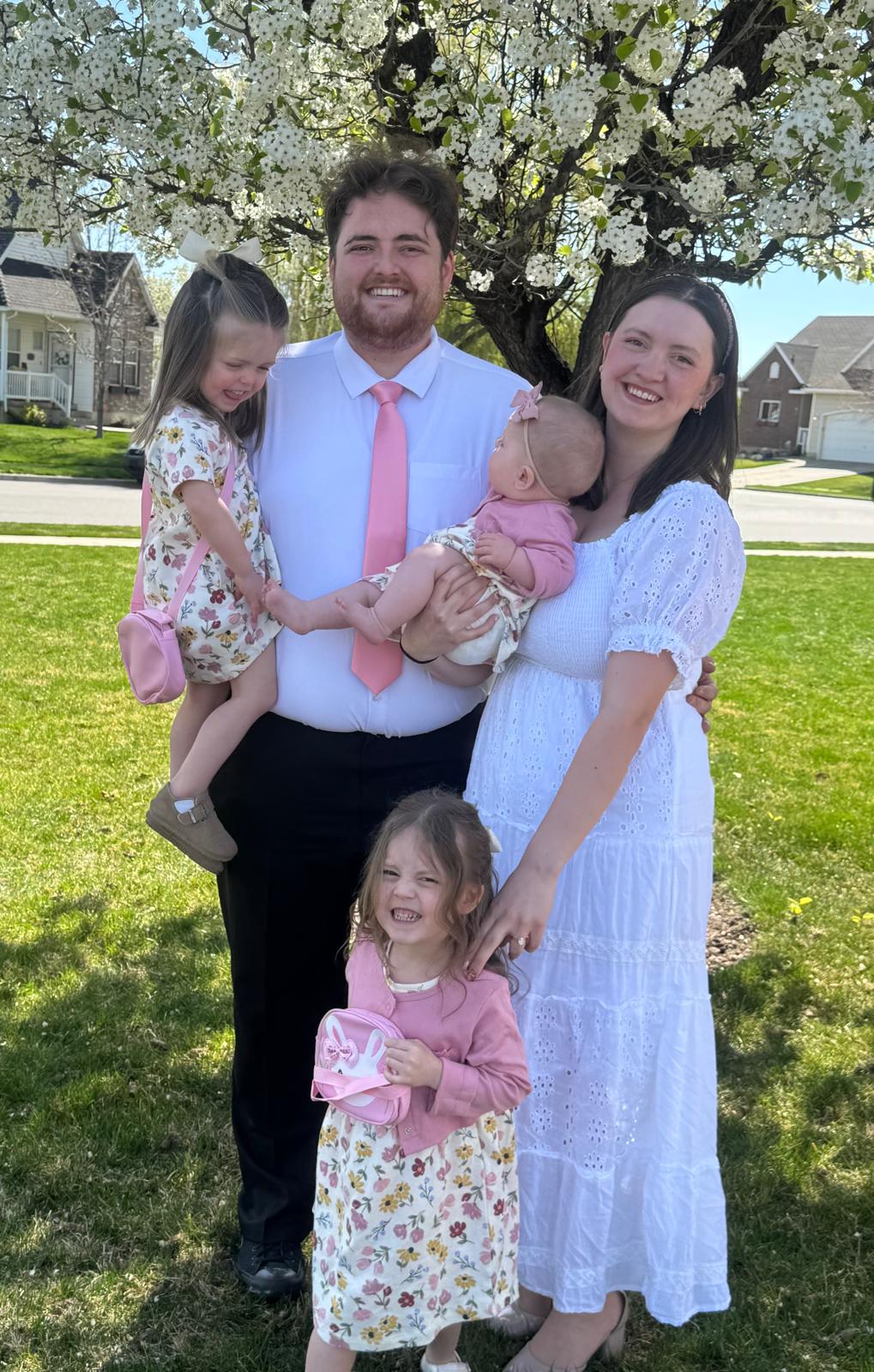 Young family of five posing under a blossoming tree on a sunny spring day