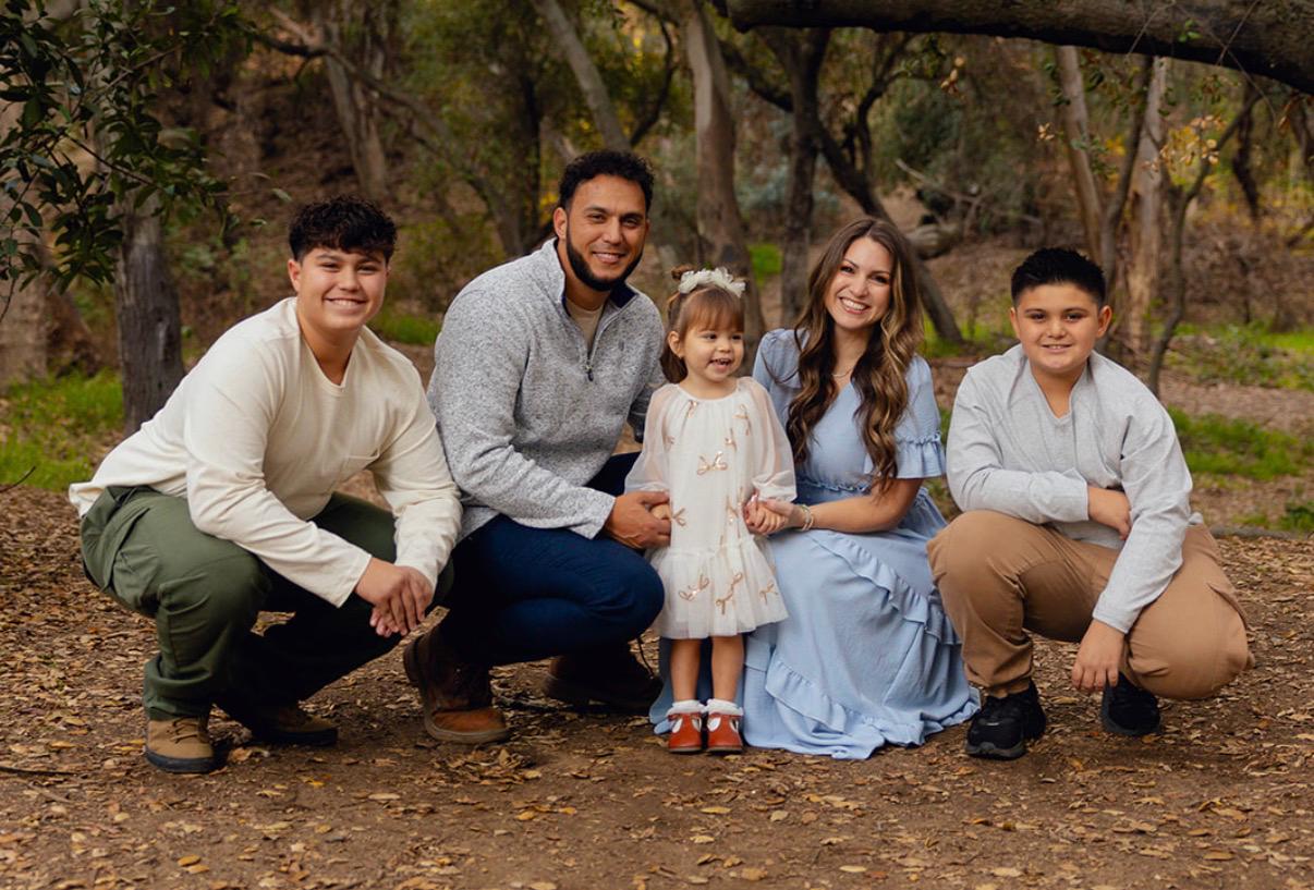 Family of five posing together outdoors under shady trees