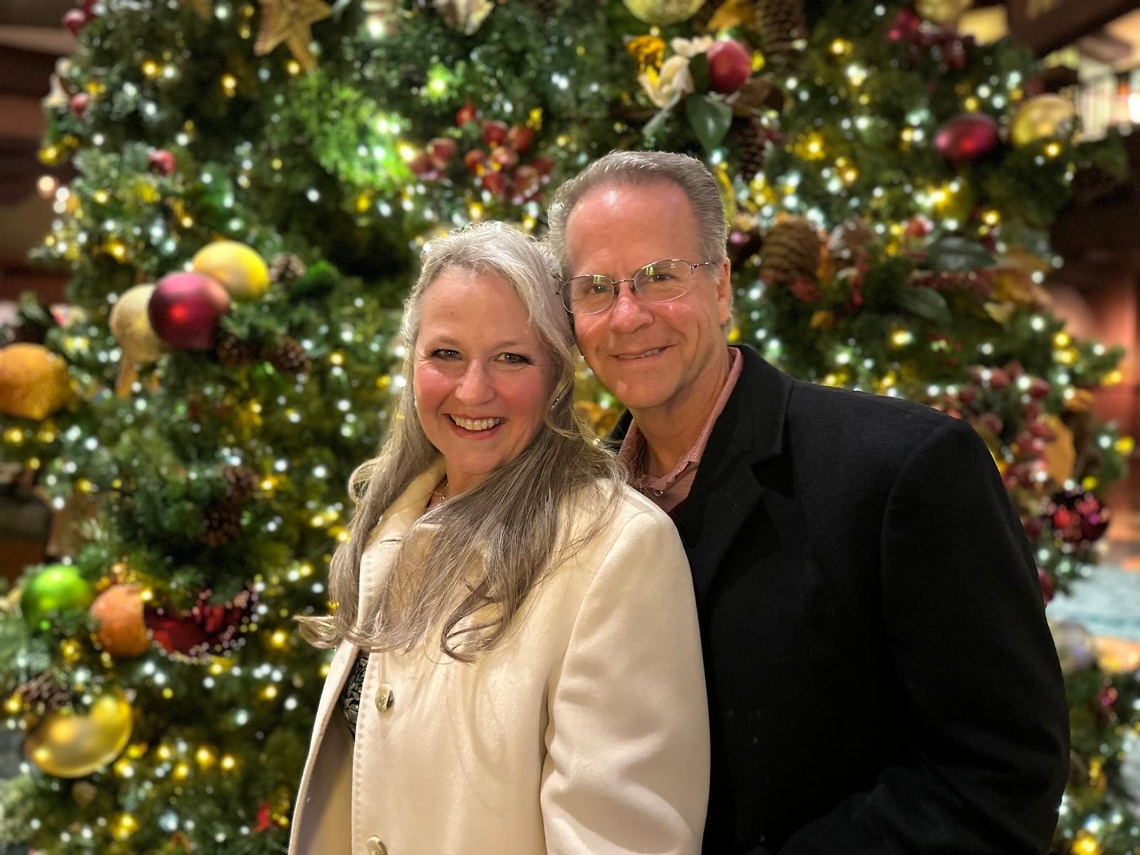Couple smiling together in front of a decorated Christmas tree